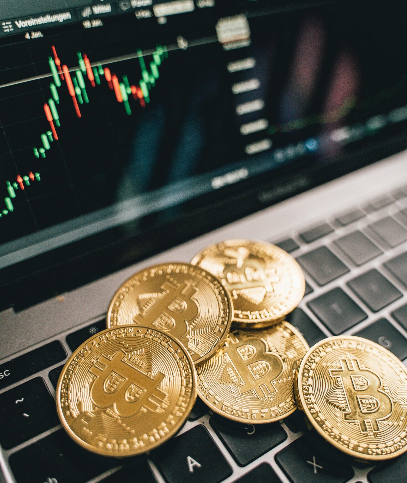 Fyzická podoba mincí Bitcoin, v pozadí graf vývoje ceny kryptoměny Bitcoin