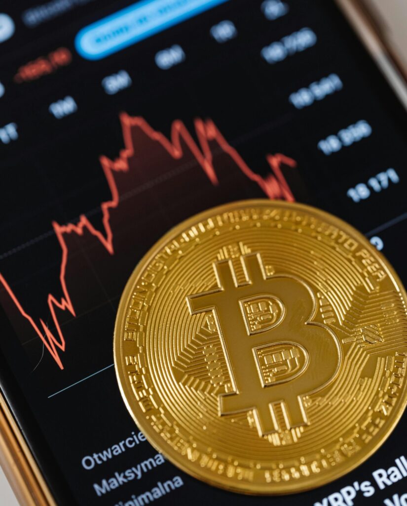 Fyzická podoba mince Bitcoin, v pozadí graf vývoje ceny kryptoměny Bitcoin
